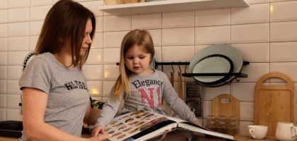 A mother and daughter enjoy reading a cookbook in a modern kitchen, sharing fun and learning together.