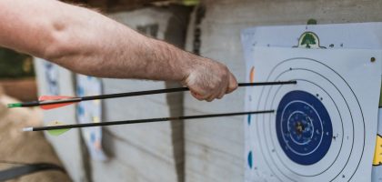 A focused arm holding arrows near a target in an archery practice setting.