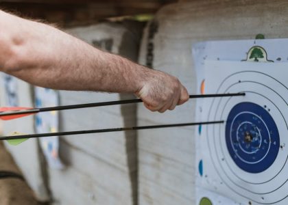 A focused arm holding arrows near a target in an archery practice setting.